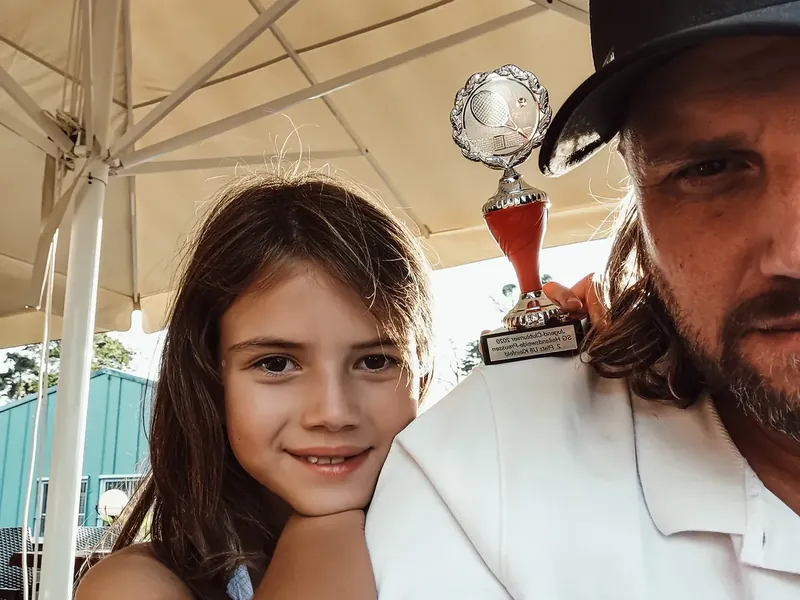 Aaliyah mit acht Jahren, das Kinn auf Gregs Schulter, darüber ihr erster Pokal