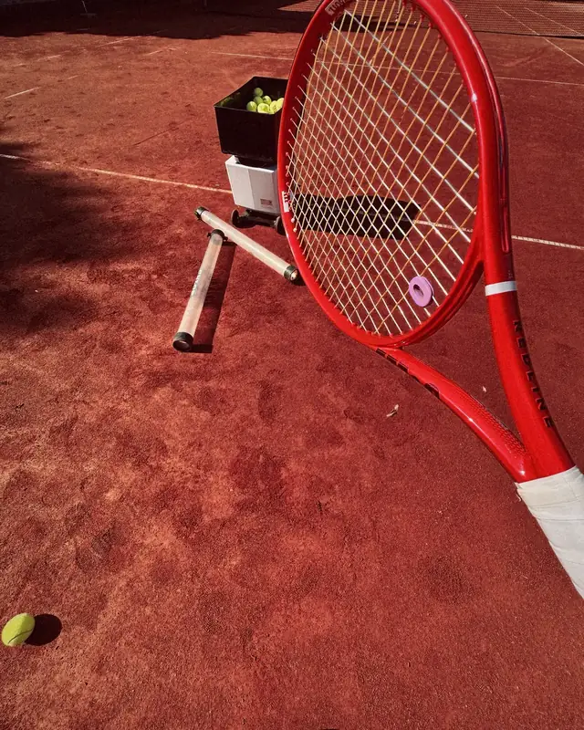 Roter Wilson-Schläger lehnt an der Ballmaschine auf dem Sandplatz