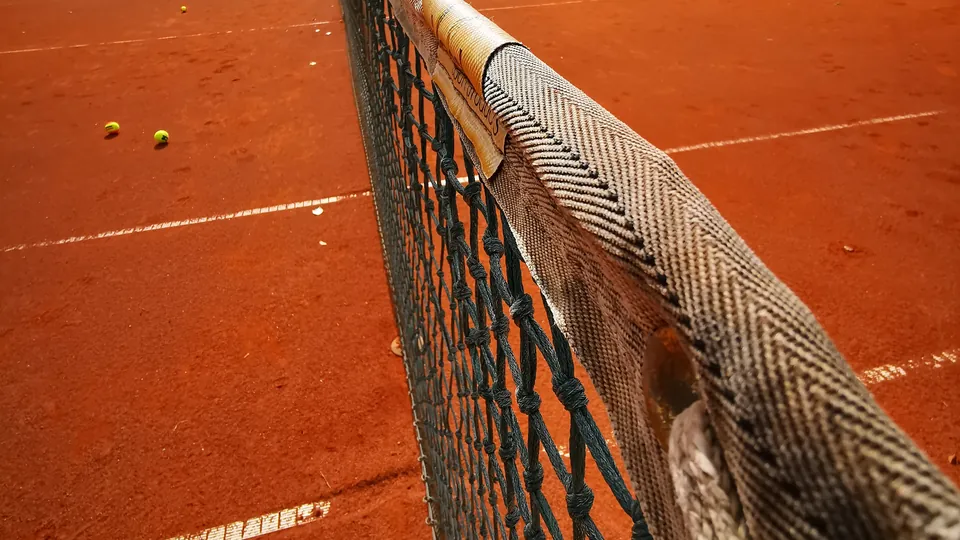 Tennisnetz auf dem Sandplatz, dahinter Bälle im Feld