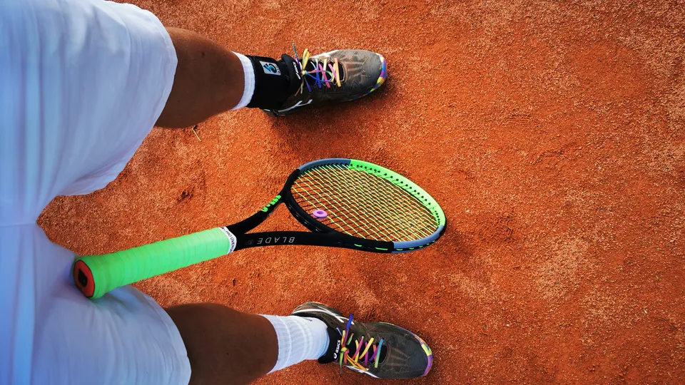Tennisschläger und Tennisschuhe auf dem Sandplatz, von oben fotografiert